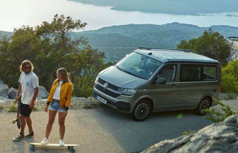 A man holding a skateboard and women standing on a skateboard infront of a campervan