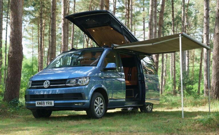 Blue campervan with roof up and awning out in woods