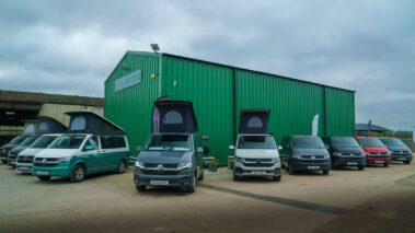 Five pop-top VW campervans and four panel vans all lined up together