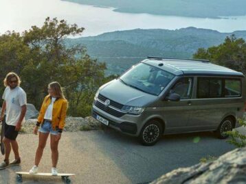 A man holding a skateboard and women standing on a skateboard infront of a campervan