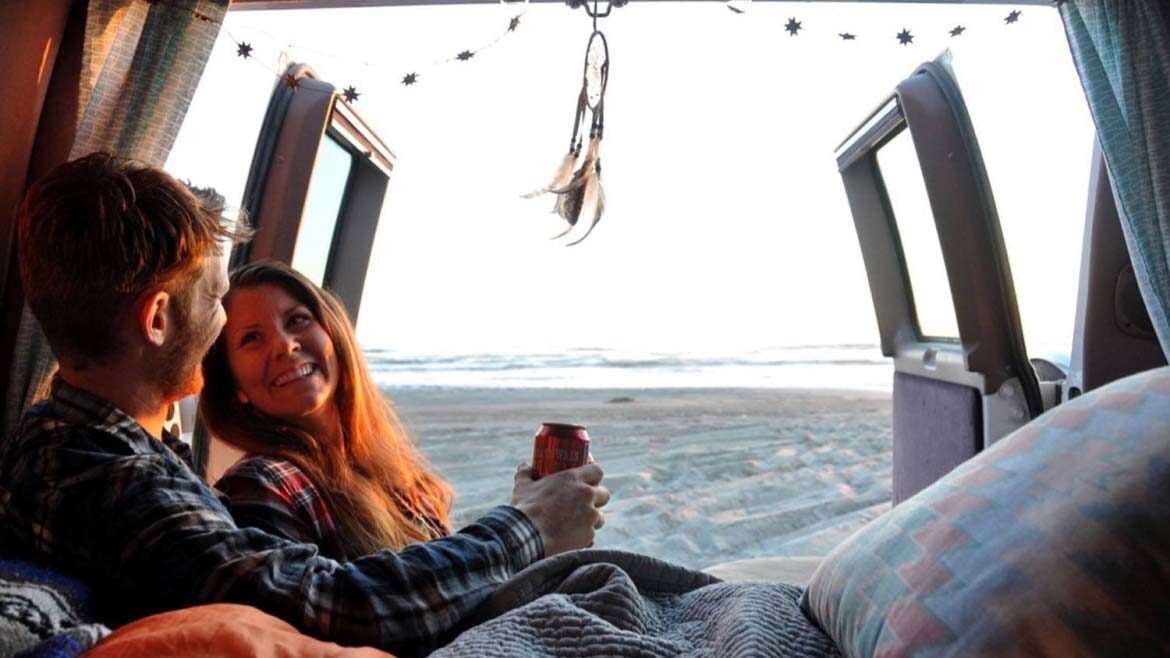 Two people lauging in a campervan under a blanket