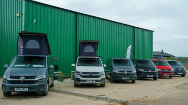 Two VW campervans with pop-tops open and four VW panel vans next to them